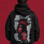 Model wearing a black Attack on Titan hoodie, back view with red Titan face breaking through a wall