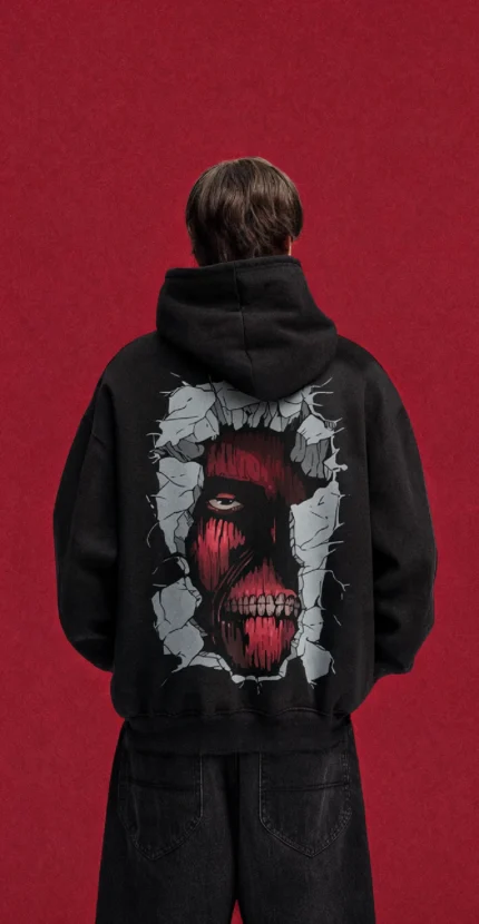 Model wearing a black Attack on Titan hoodie, back view with red Titan face breaking through a wall